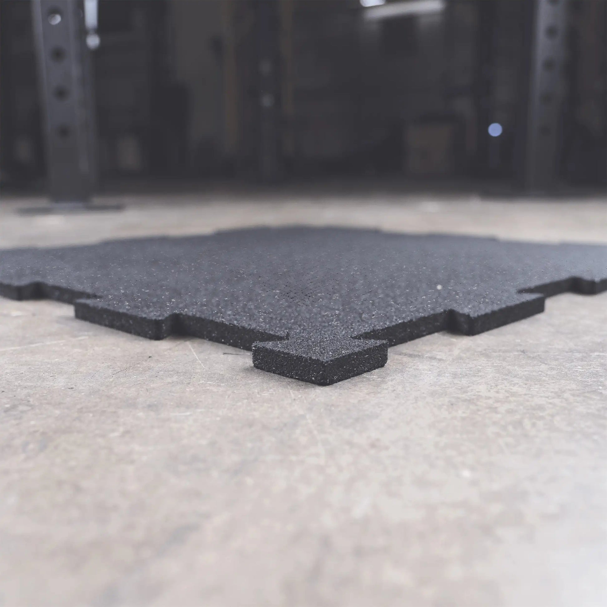 Black interlocking rubber gym flooring tile on concrete surface.
