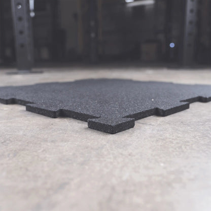 Black interlocking rubber gym flooring tile on concrete surface.
