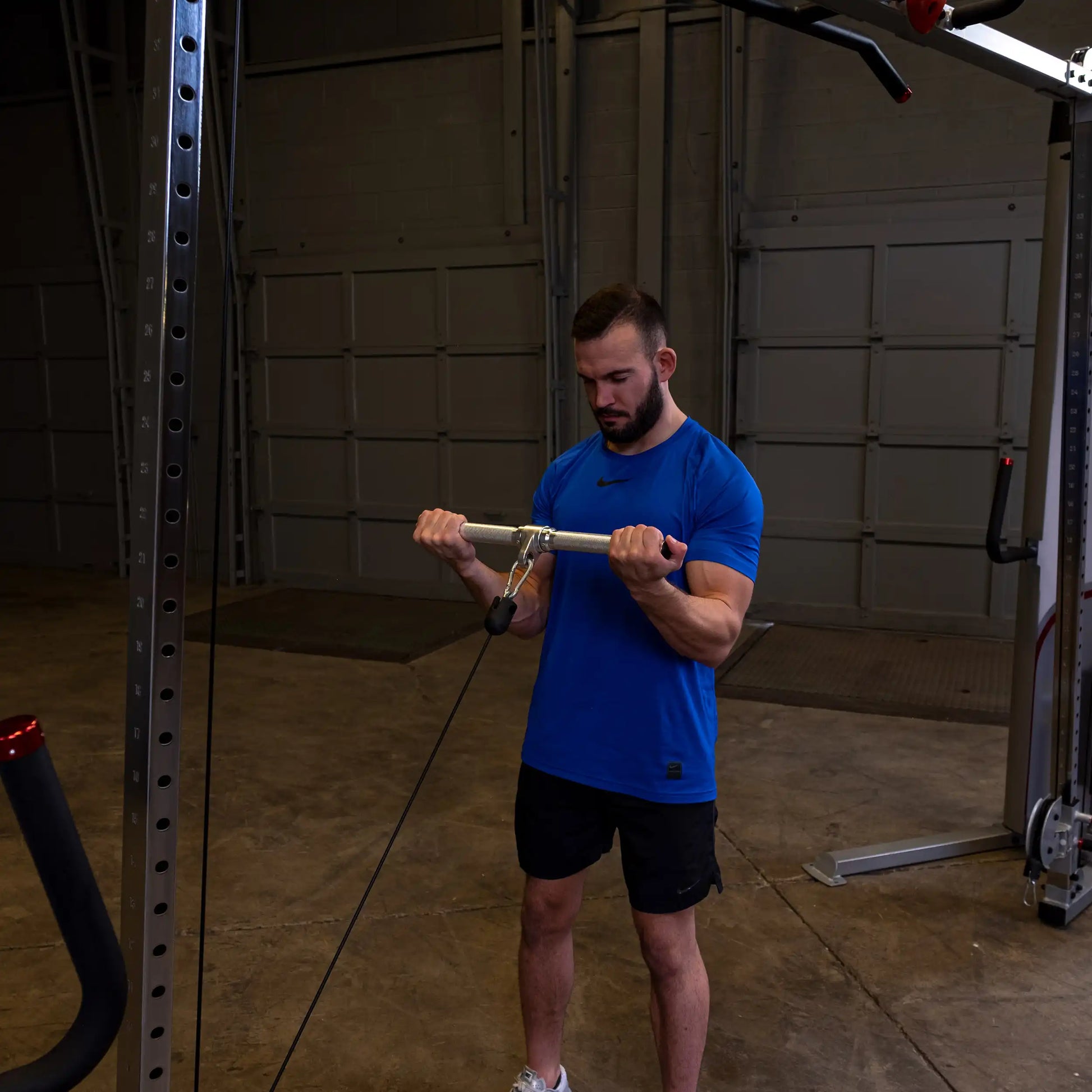 Man in blue shirt using cable machine for bicep curls in a gym.