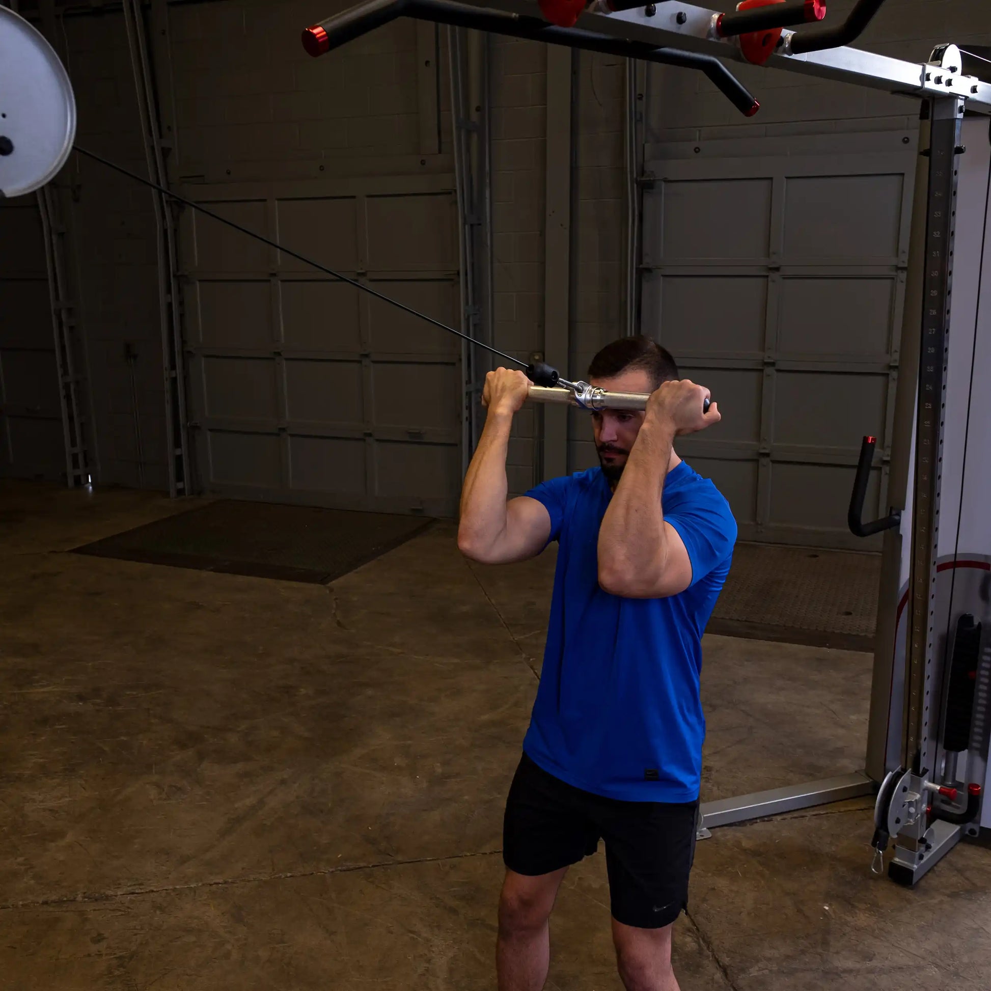Man in blue shirt exercising with cable machine in garage gym.