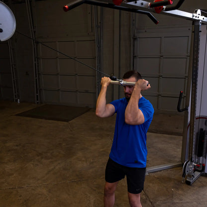 Man in blue shirt exercising with cable machine in garage gym.