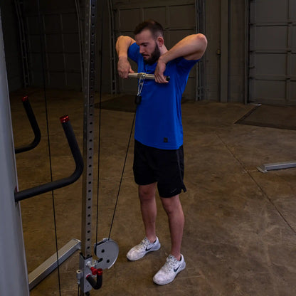 Man in blue shirt using cable machine for tricep workout in gym.