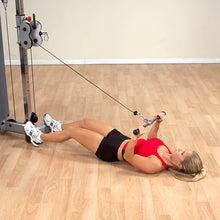 Woman performing cable pullover exercise on a machine in a red top and black shorts.