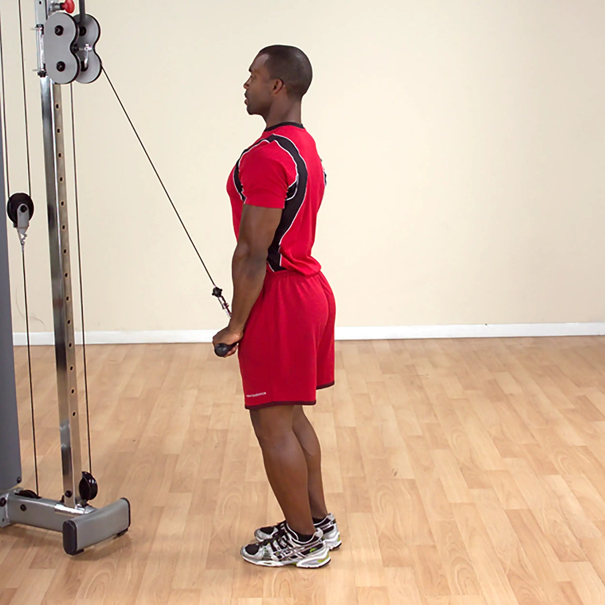 Man in red sportswear performing tricep cable pushdown in gym.