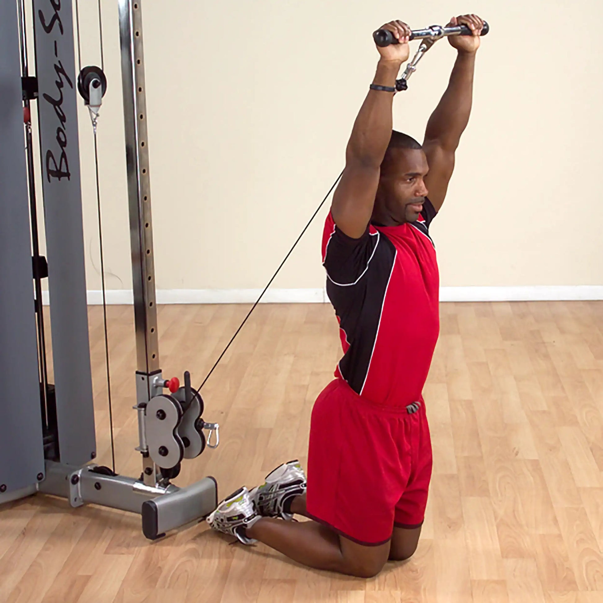 Man in red workout attire performing triceps exercise on cable machine in gym.