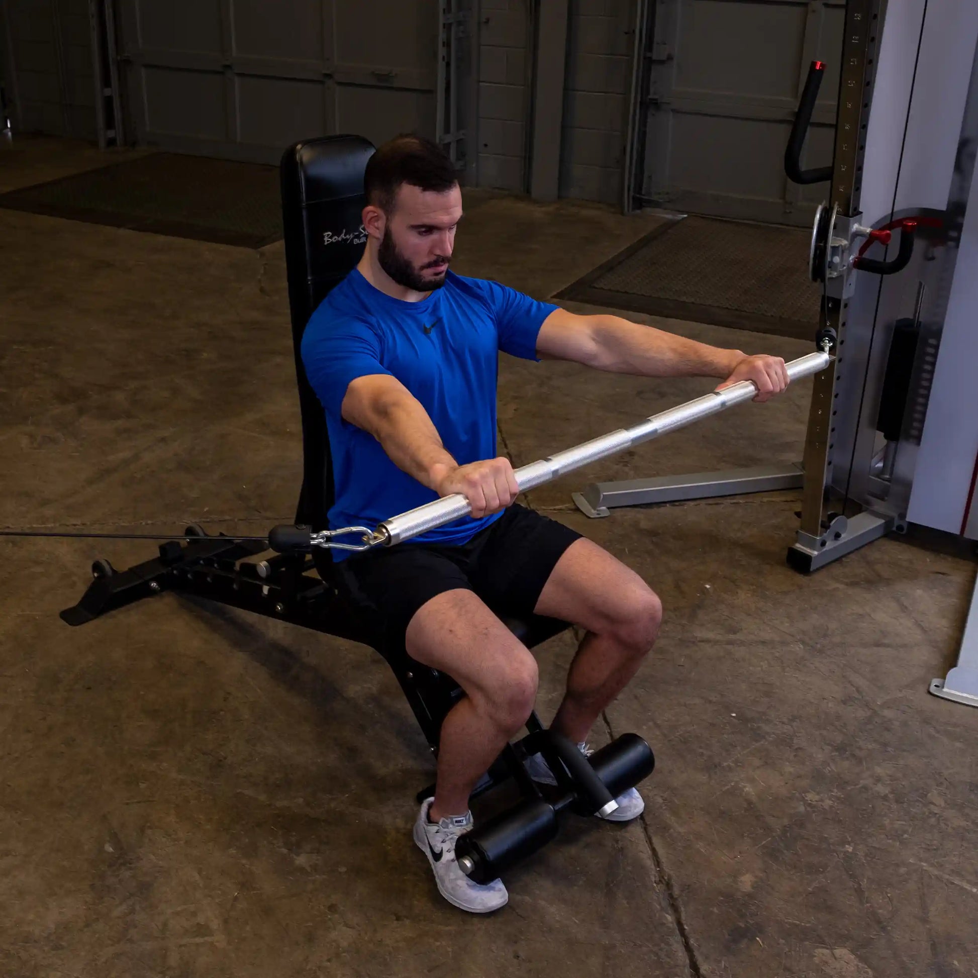 Man in blue shirt using Body-Solid machine for seated cable row exercise.