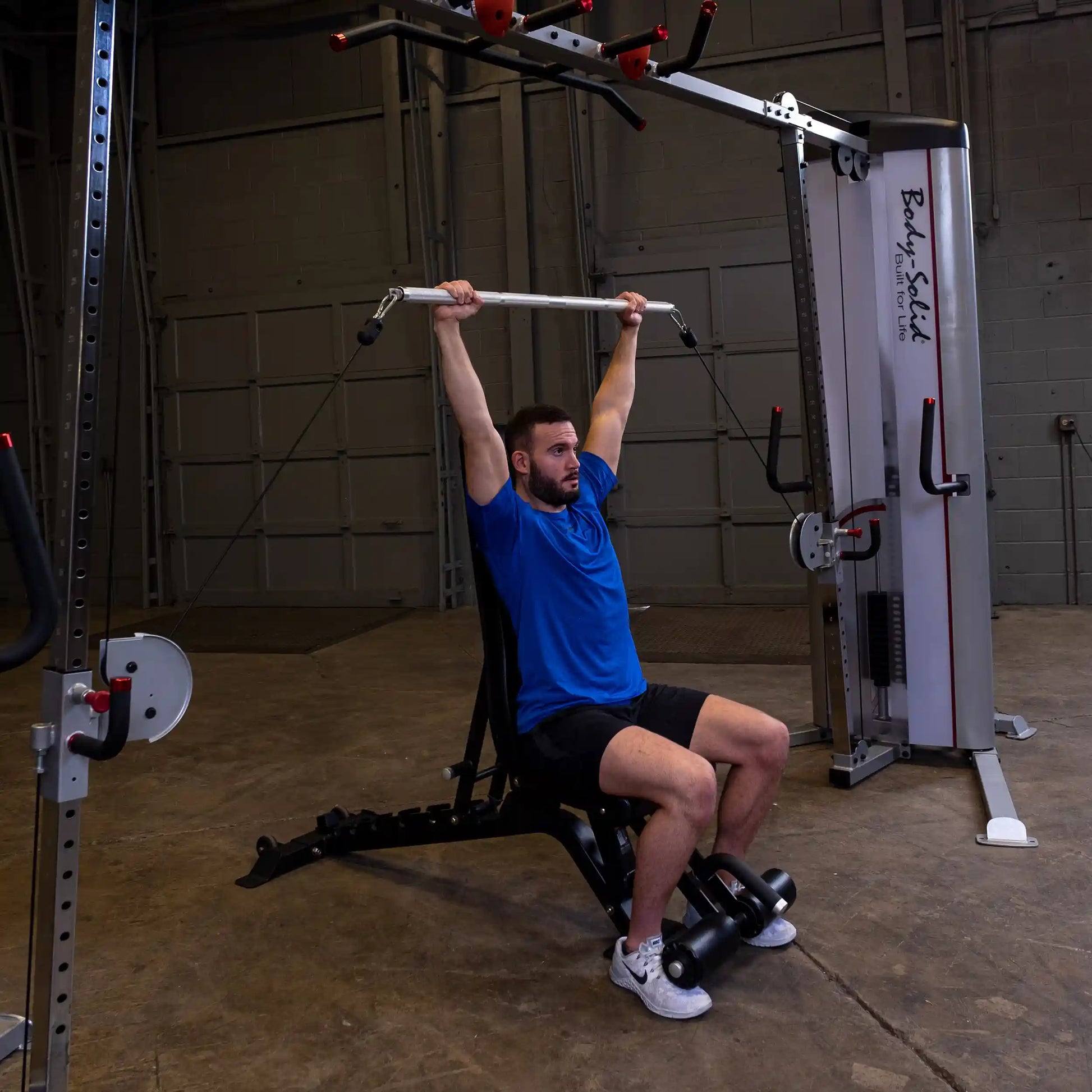 Man using Body-Solid lat pulldown machine in gym, wearing a blue shirt.