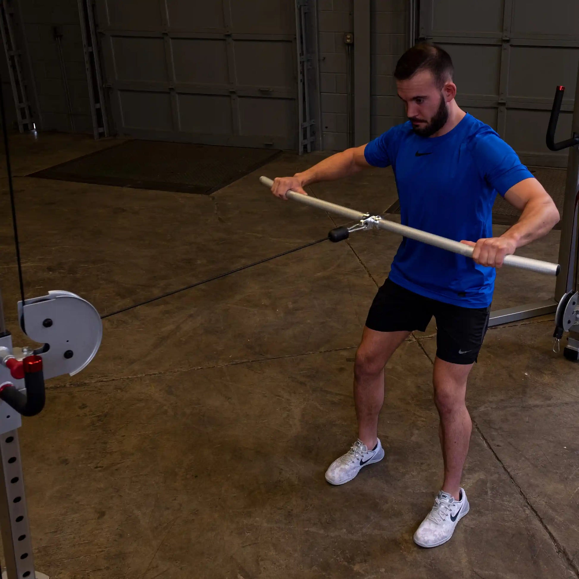 Man in blue shirt using cable machine with wooden bar for strength training.