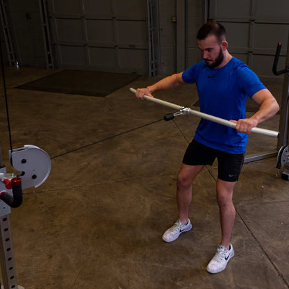 Man in blue shirt using cable machine with wooden bar for strength training.