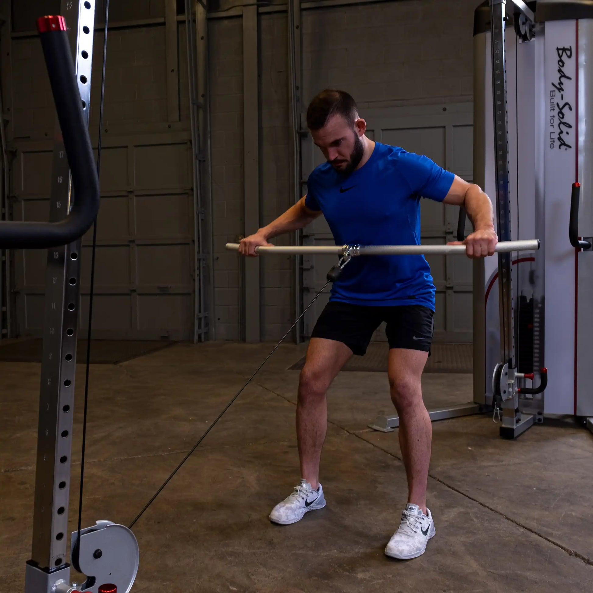 Man in blue shirt uses Body-Solid cable machine for exercise in gym.