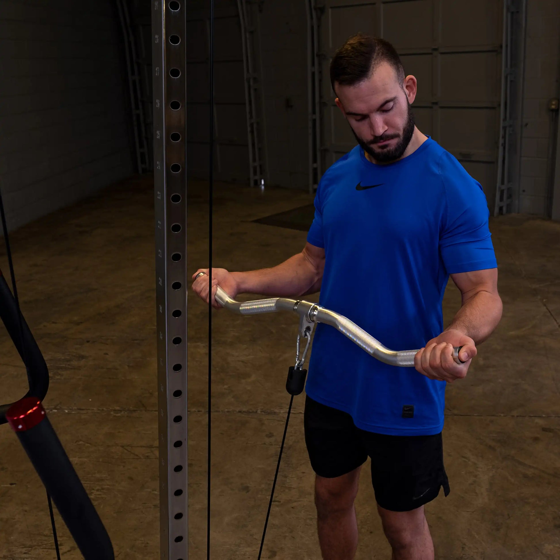 Man in blue Nike shirt using cable machine for bicep curls in a gym.