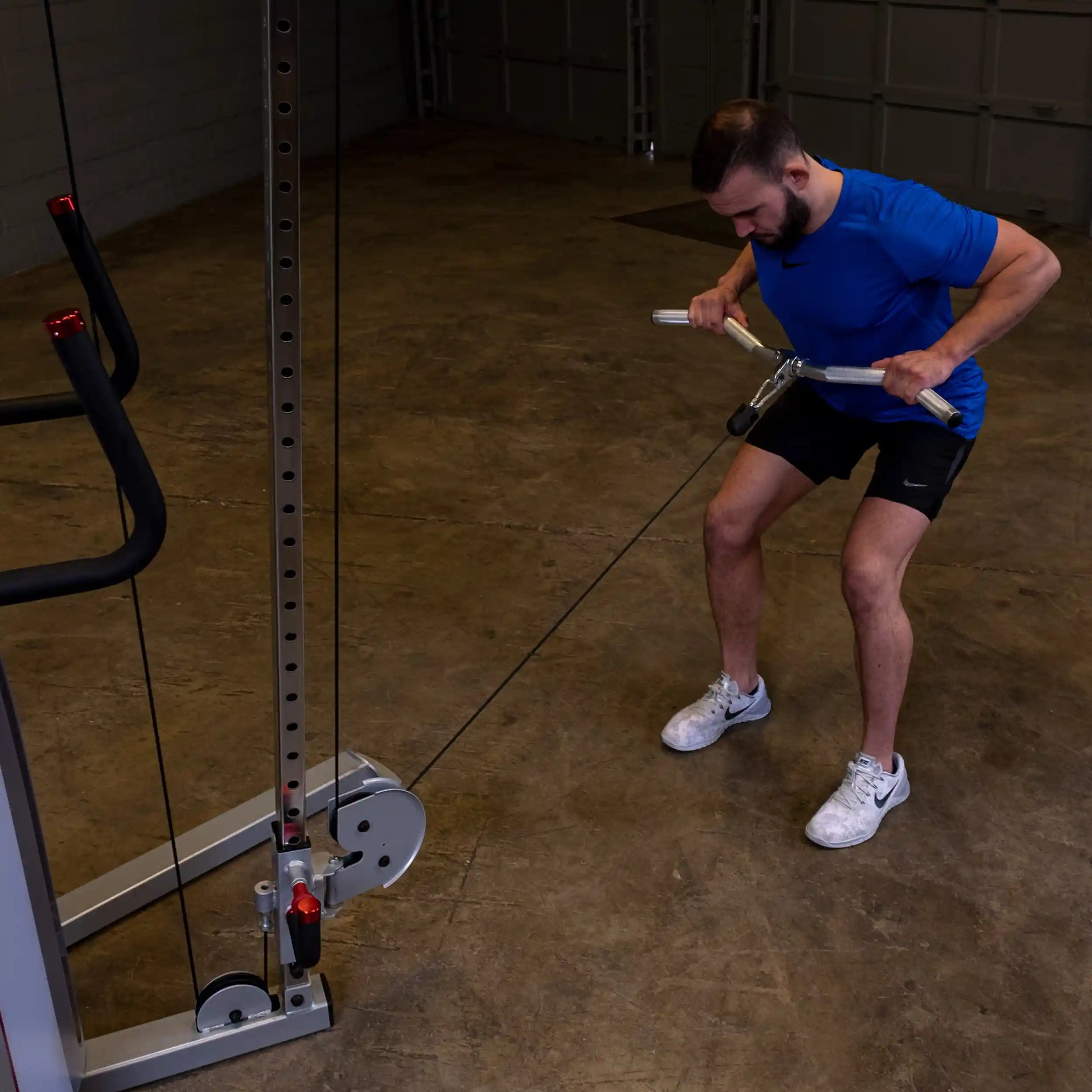 Man in blue shirt using cable machine for back workout in gym.