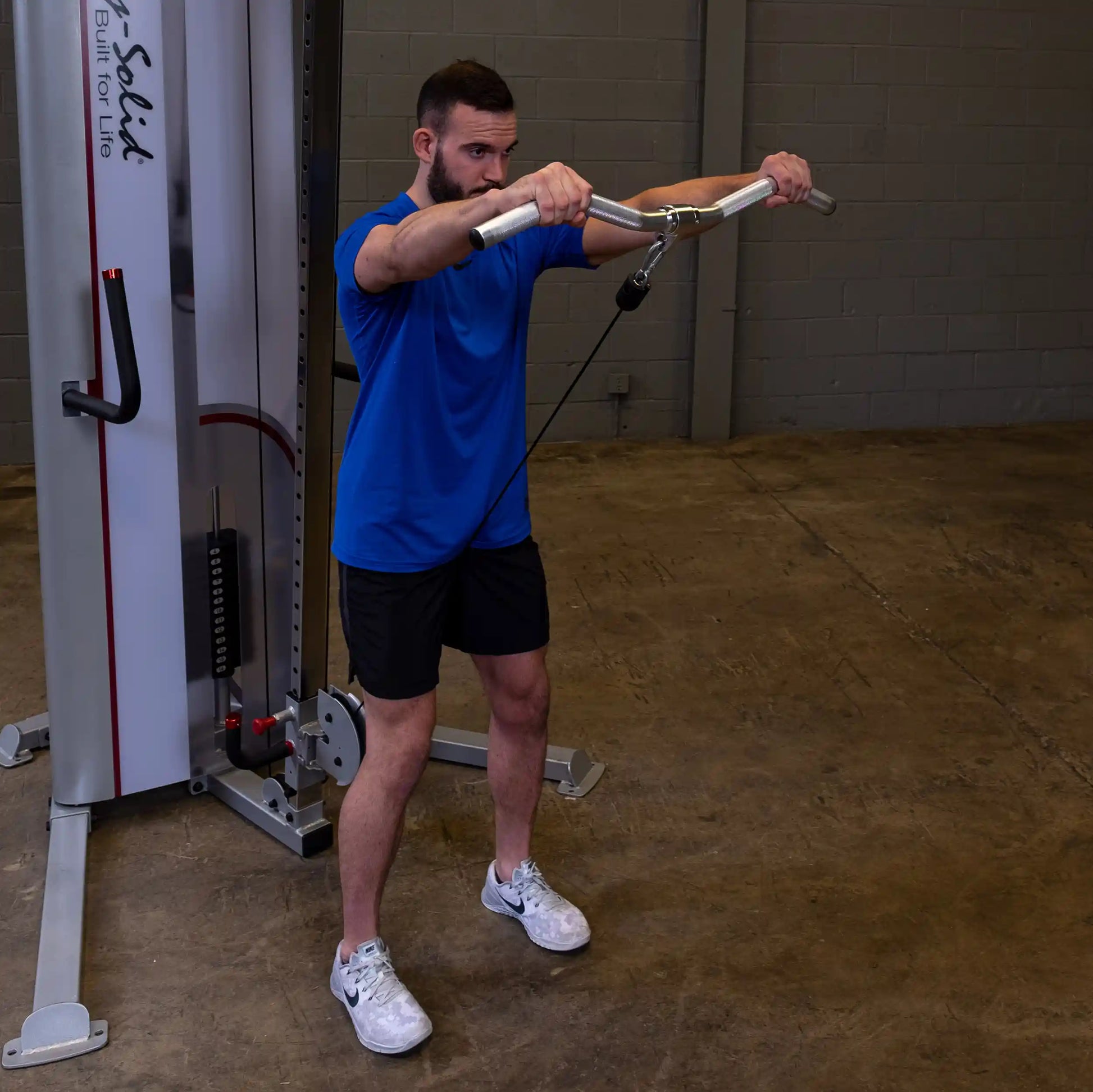 Man in blue shirt using Body-Solid cable machine in gym for strength training.
