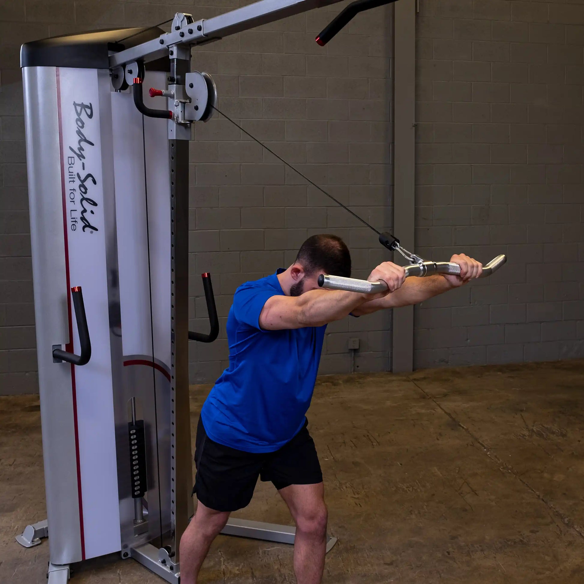 Man using Body-Solid cable machine in blue shirt for tricep exercise.