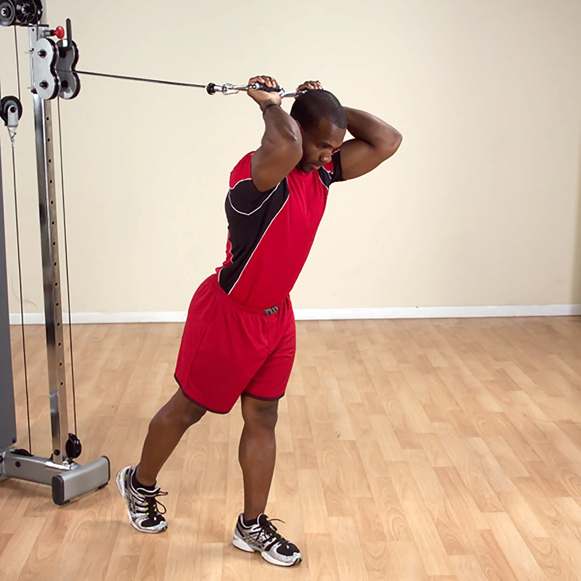 Man performing tricep cable extension in red sportswear at gym.
