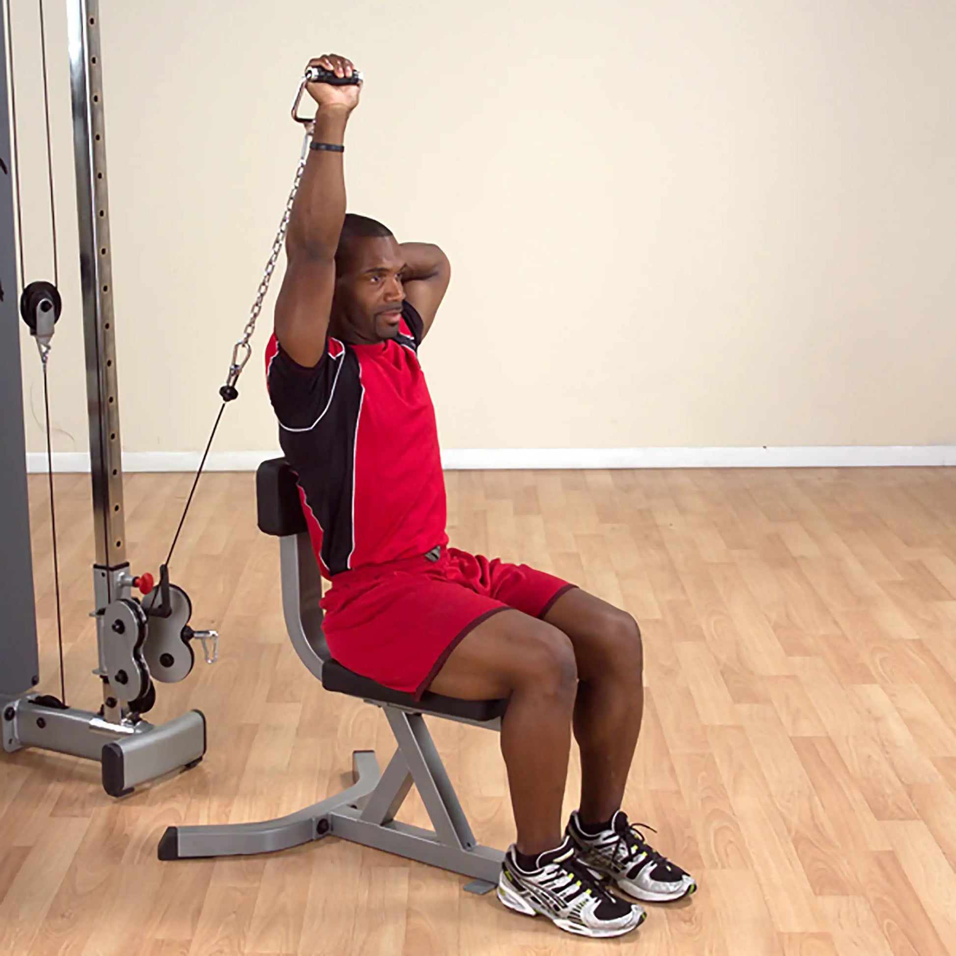 Man in red athletic outfit using a cable machine for tricep exercise in a gym.