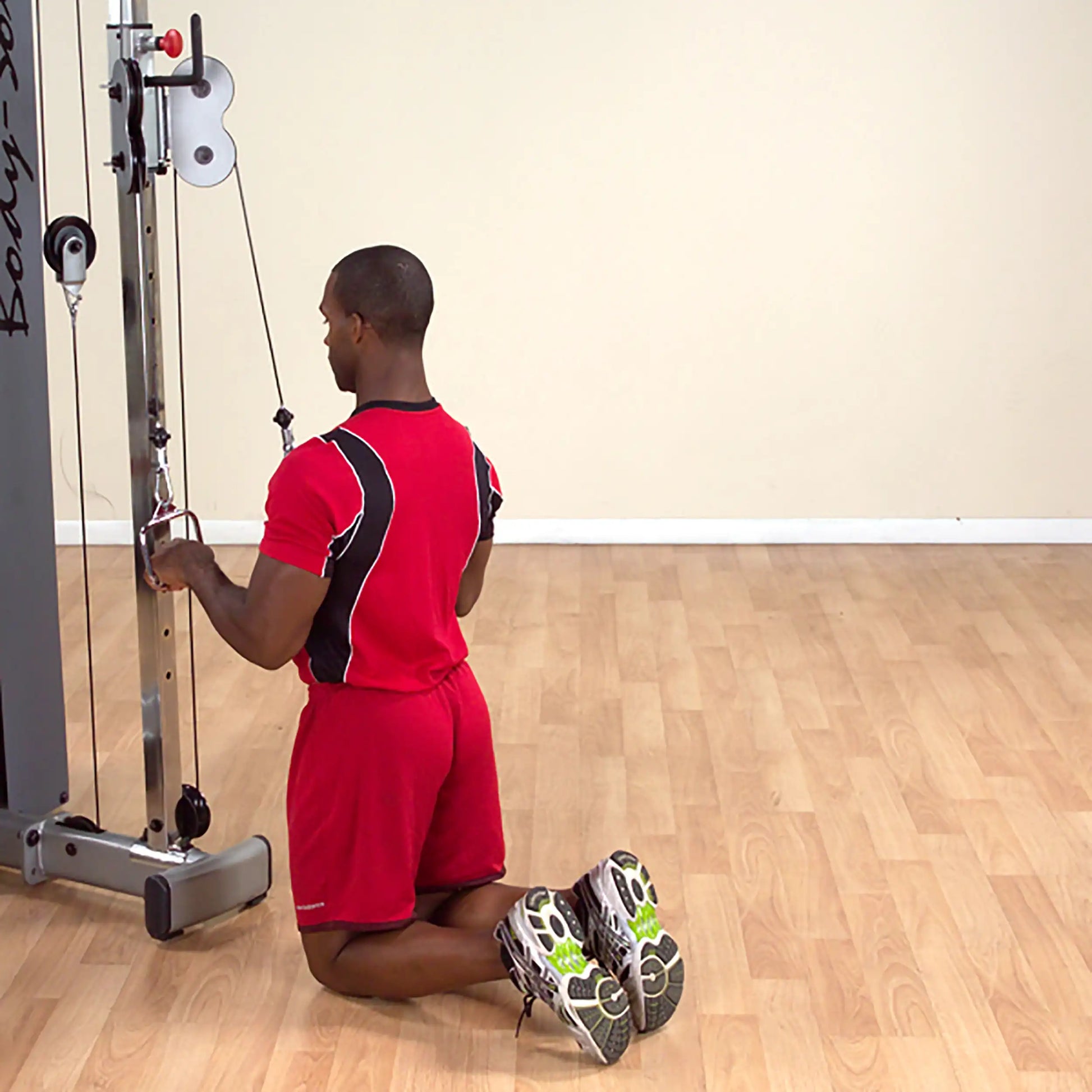 Man in red workout gear performing tricep pushdown on cable machine.