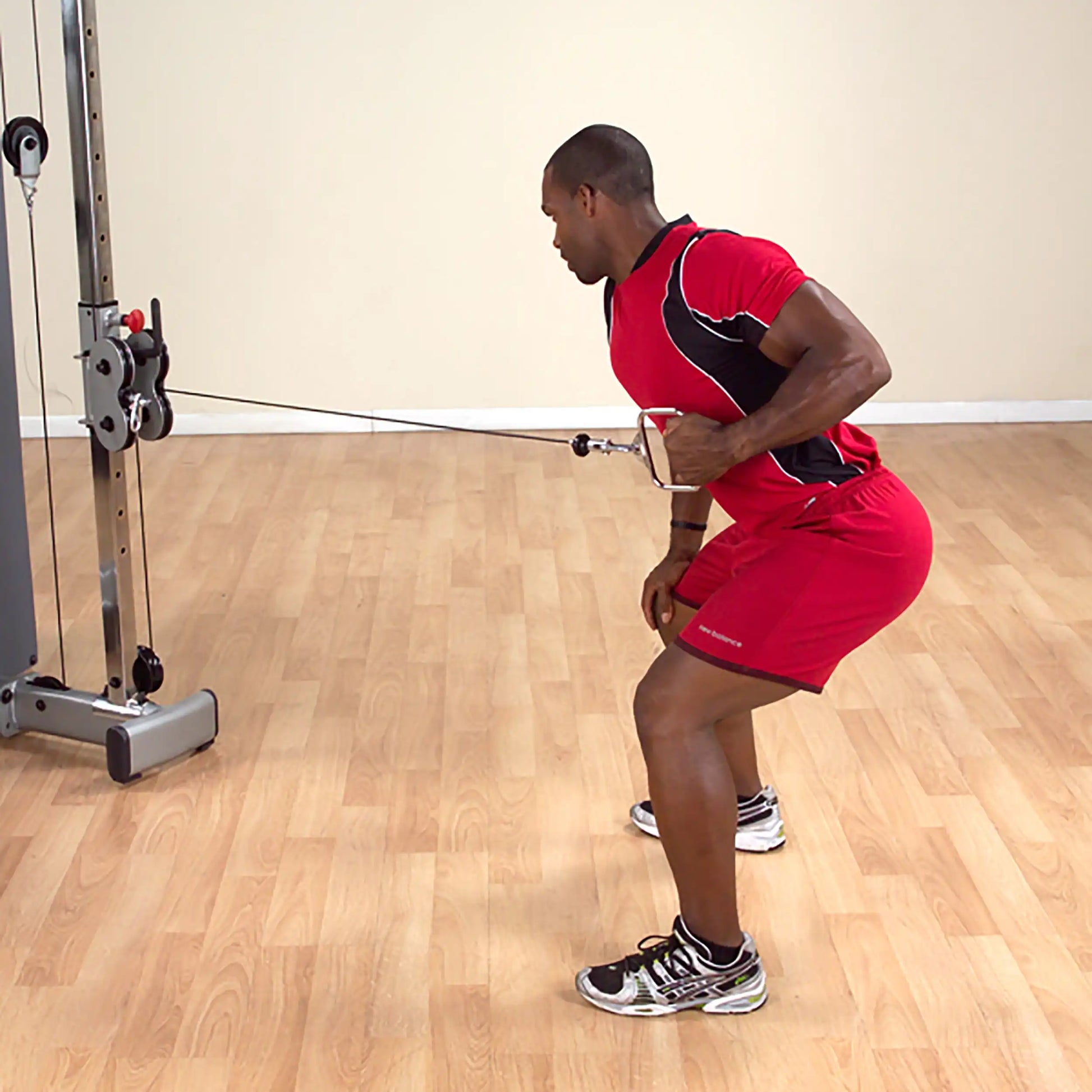 Man performing cable row exercise in red athletic wear on wood floor.
