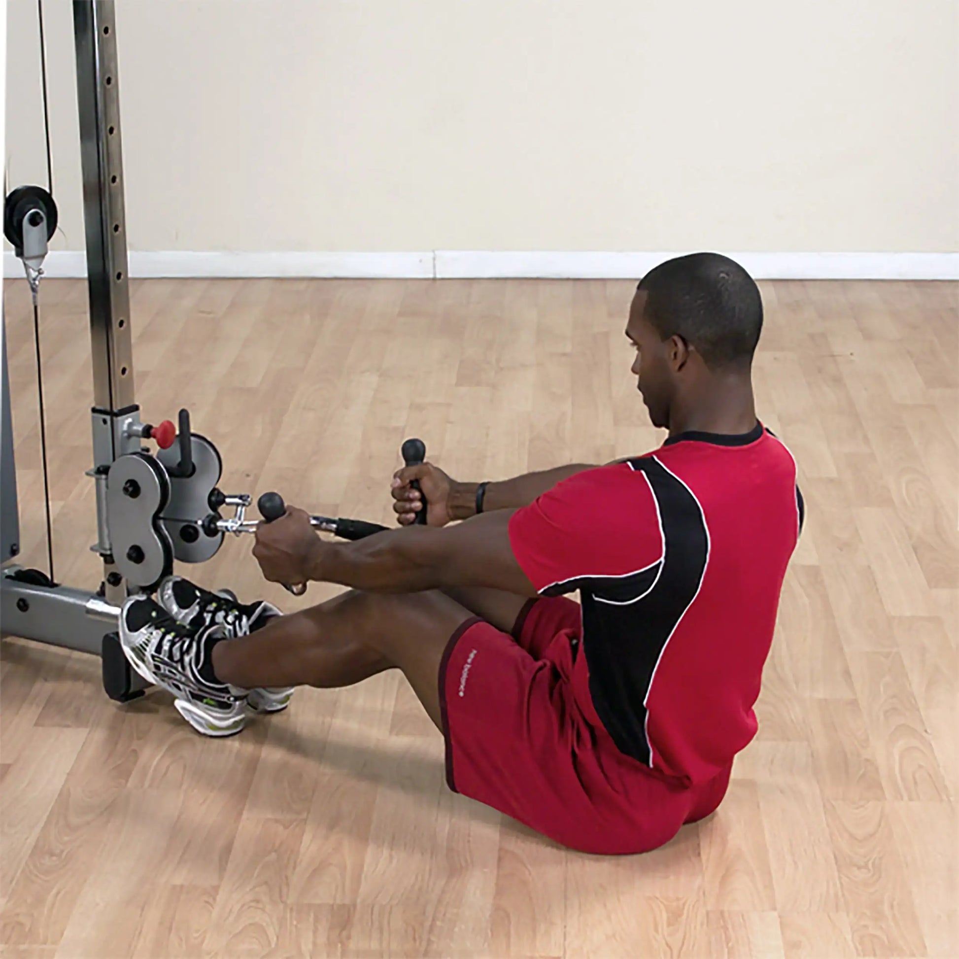 Man in red workout attire using a cable machine for seated rows in a gym.