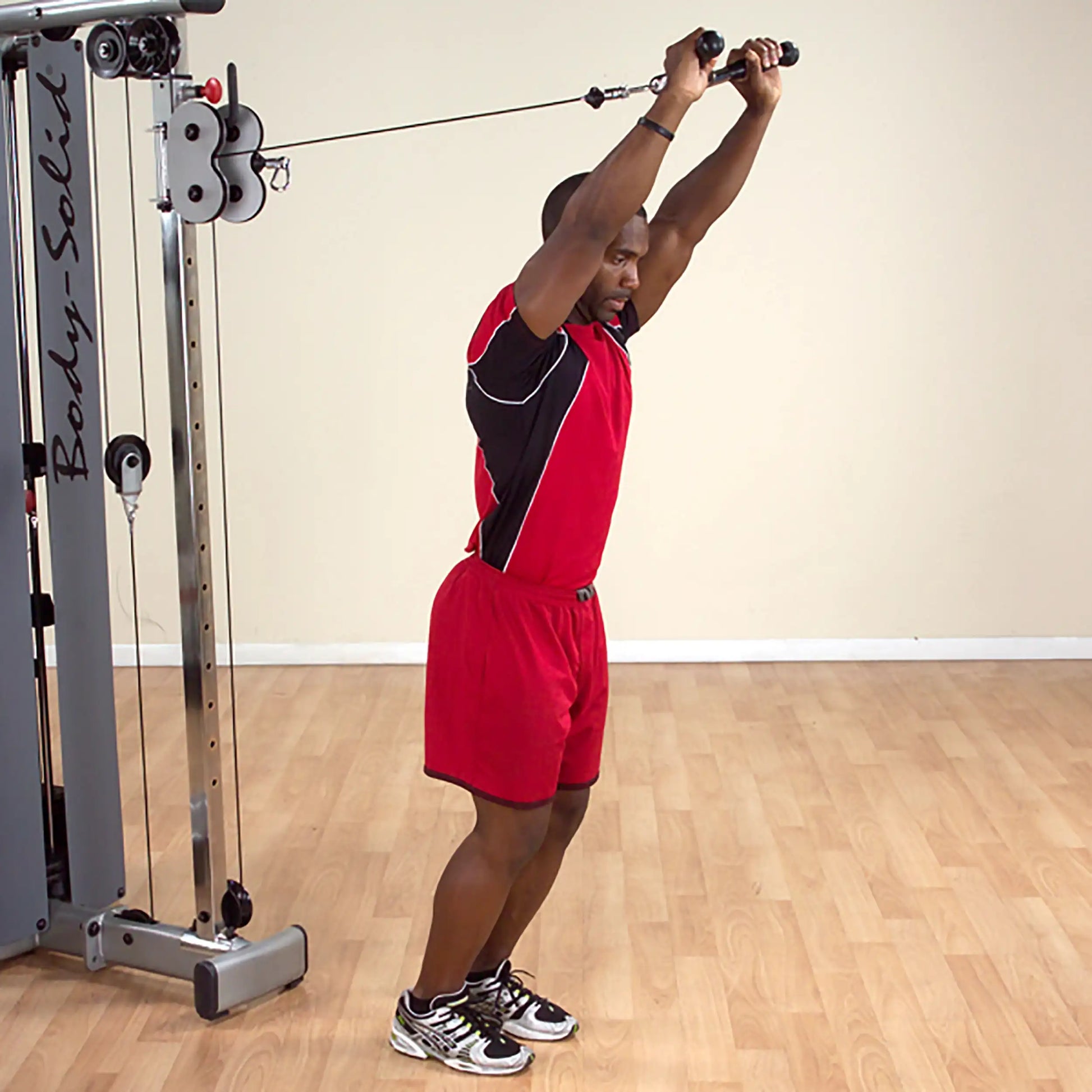 Man performing tricep extension on Body-Solid cable machine, wearing red athletic outfit.