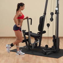 Woman using a cable machine for leg exercises in a home gym.