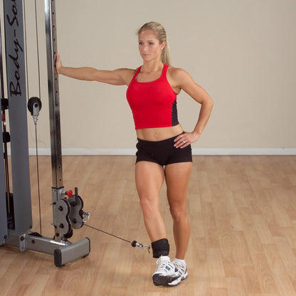 Woman in red top using cable machine for leg workout in gym.
