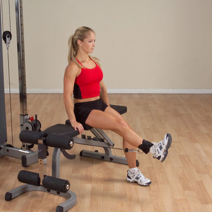 Woman performing leg extension exercise on gym machine in red top and black shorts.