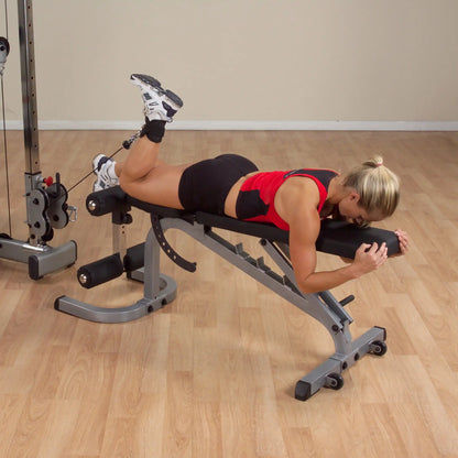 Woman in red top using leg curl machine for hamstring workout at gym.