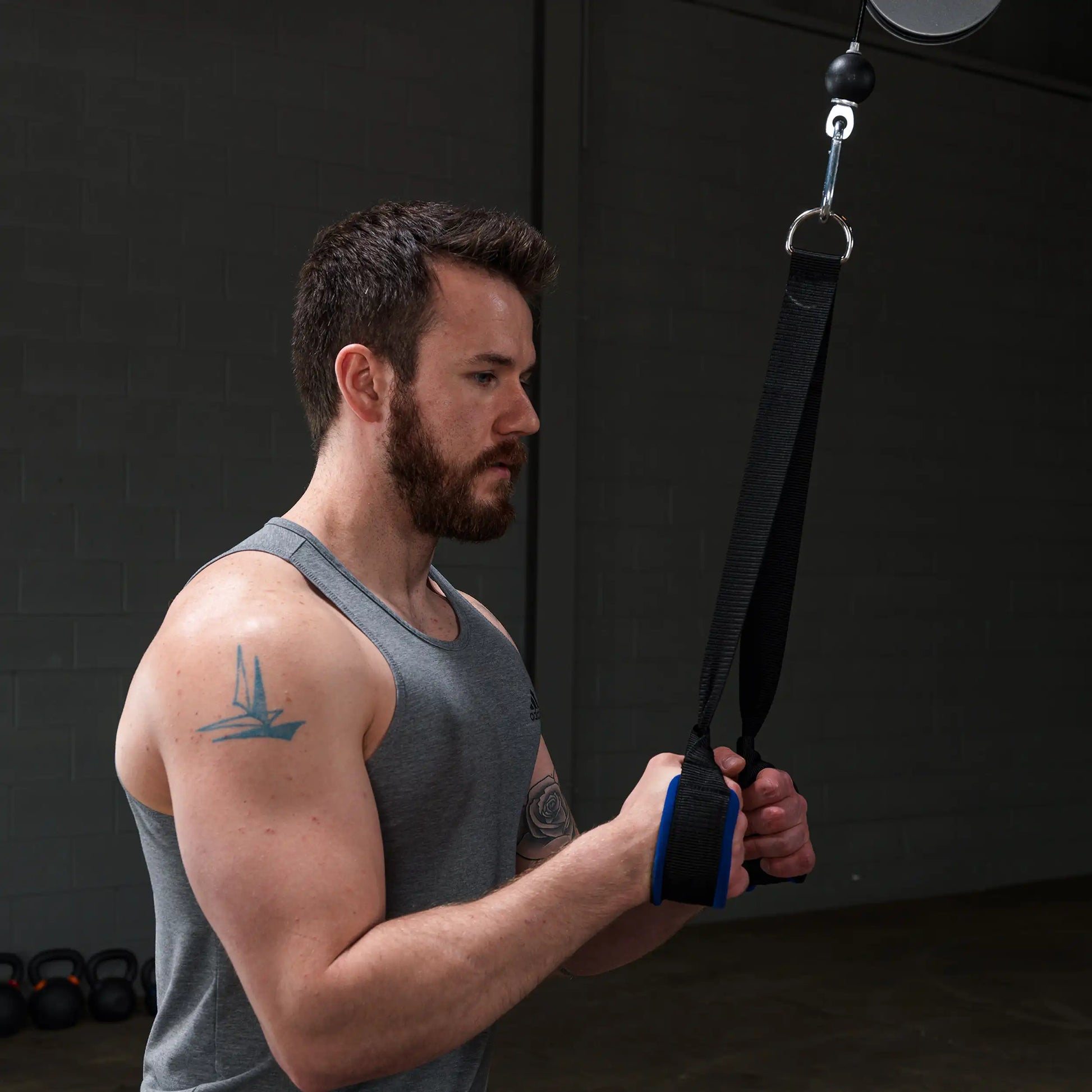 Man using black resistance bands in gym, wearing gray tank top with arm tattoo.