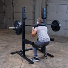 Man performing barbell squat on black squat rack in a gym.