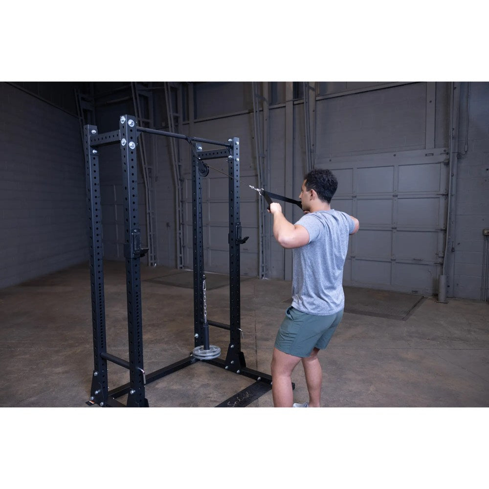 Man using a black Rogue Fitness power rack with pulley in a gym.