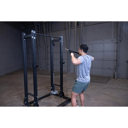 Man using a black Rogue Fitness power rack with pulley in a gym.