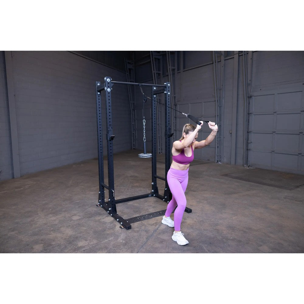 Woman exercising on a black cable machine in a gym, wearing a pink workout outfit.