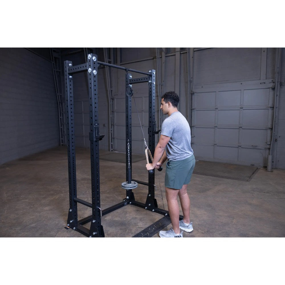 Man using a black power rack for cable tricep pushdowns in a garage gym.