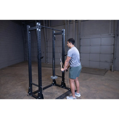 Man using a black power rack for cable tricep pushdowns in a garage gym.