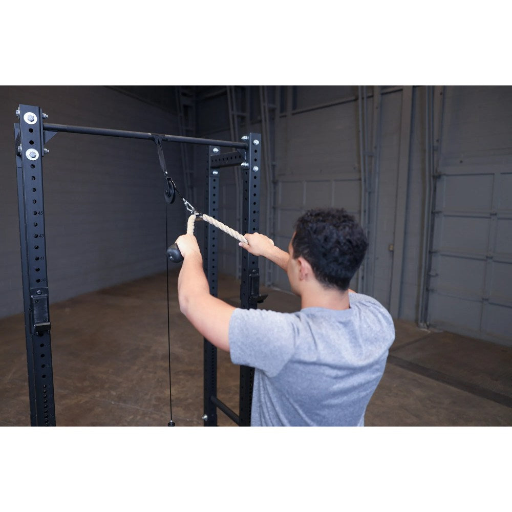 Man using a rope pull-down attachment on a black power rack in a gym.