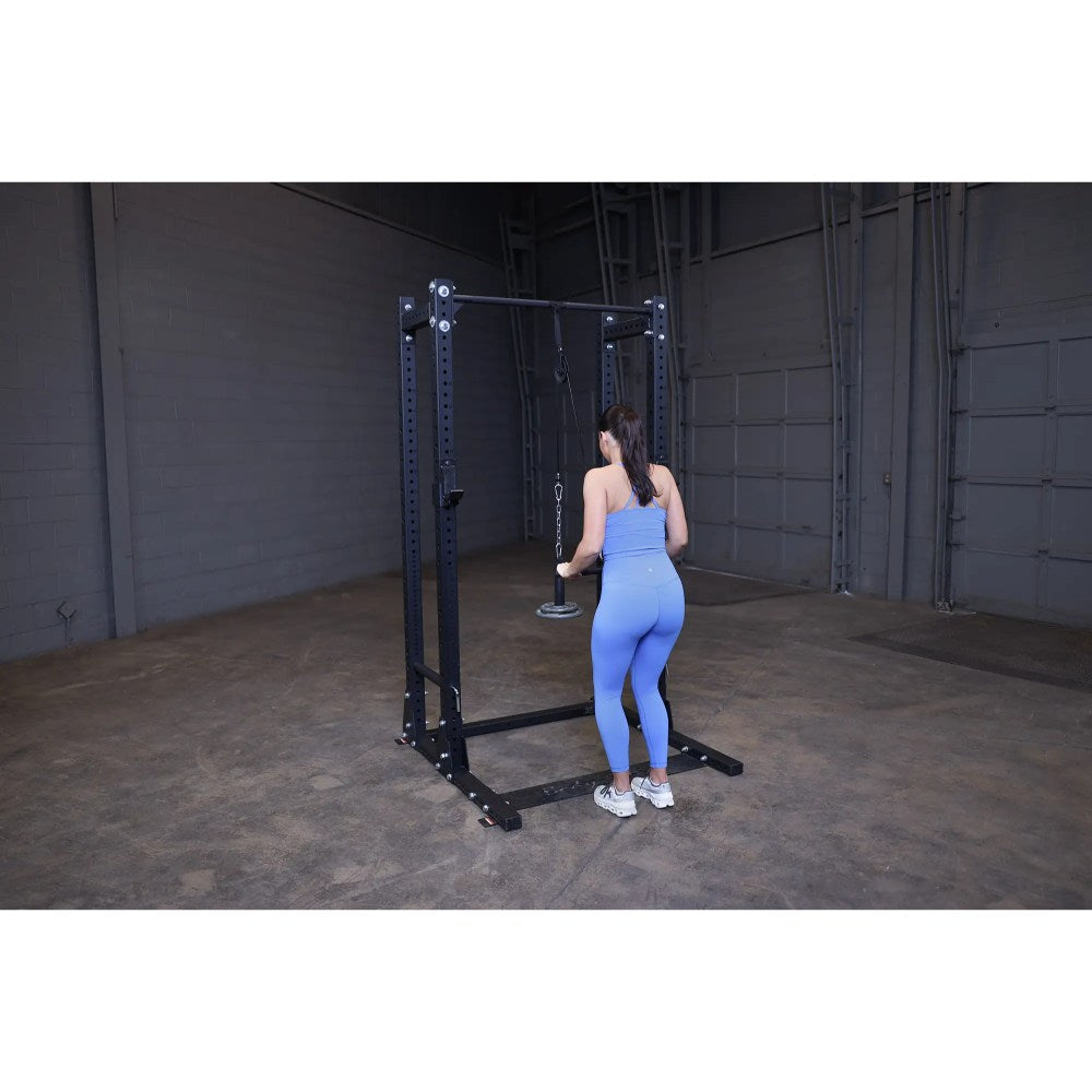 Woman using a black cable machine in a gym, wearing blue workout leggings.