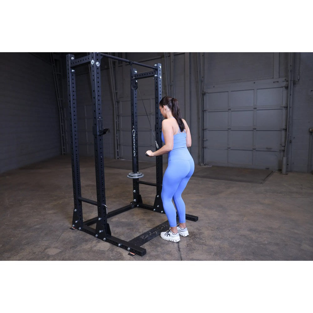 Woman in blue activewear using a black home gym power rack for strength training.