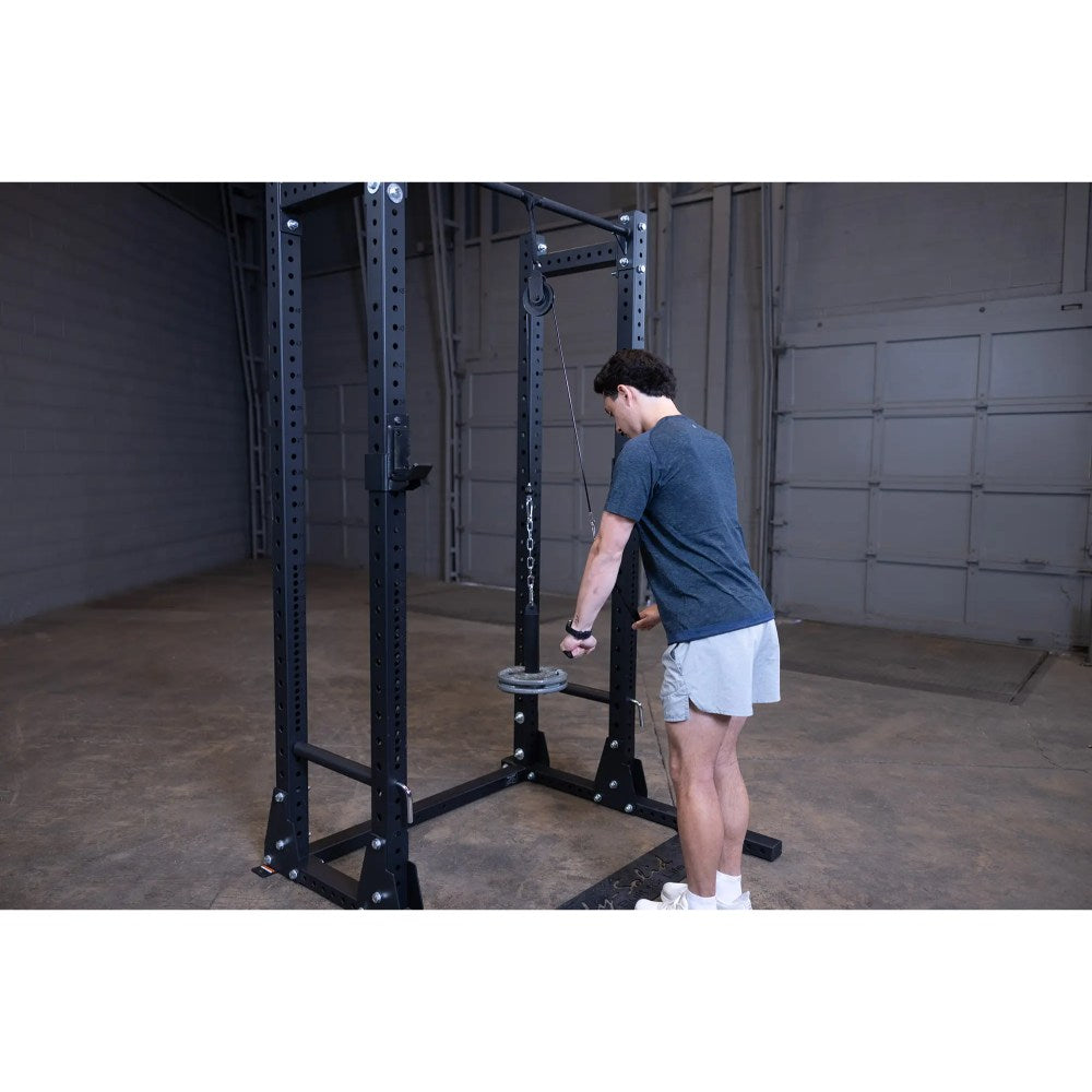 Man using black power rack with pulley system for tricep workout in garage gym.