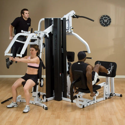 Body-Solid home gym with three people exercising on a multi-station machine in a fitness room.