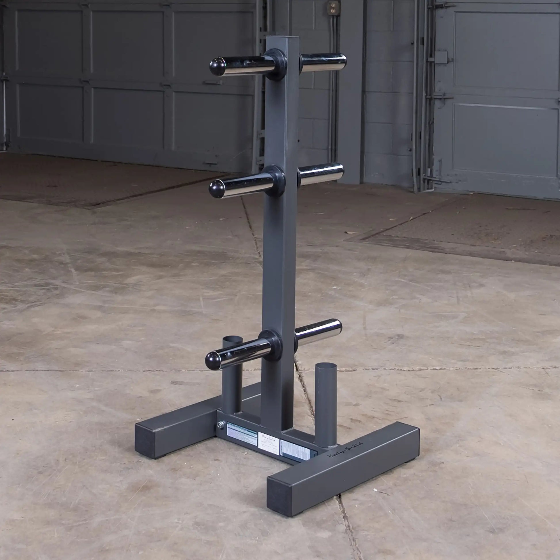 Steel weight plate tree rack with four storage pegs in a garage gym setting.
