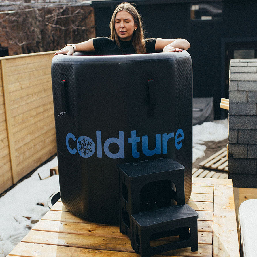 A person preparing to use the Coldture Barrel + Chiller Pro, a portable cold therapy tub, set on a wooden platform outdoors.