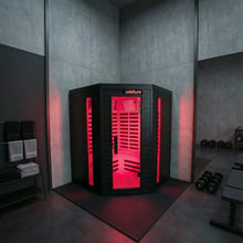 Black corner infrared sauna with bright red interior lighting and horizontal bench seating, installed in a modern gym with concrete walls and dumbbells nearby.
