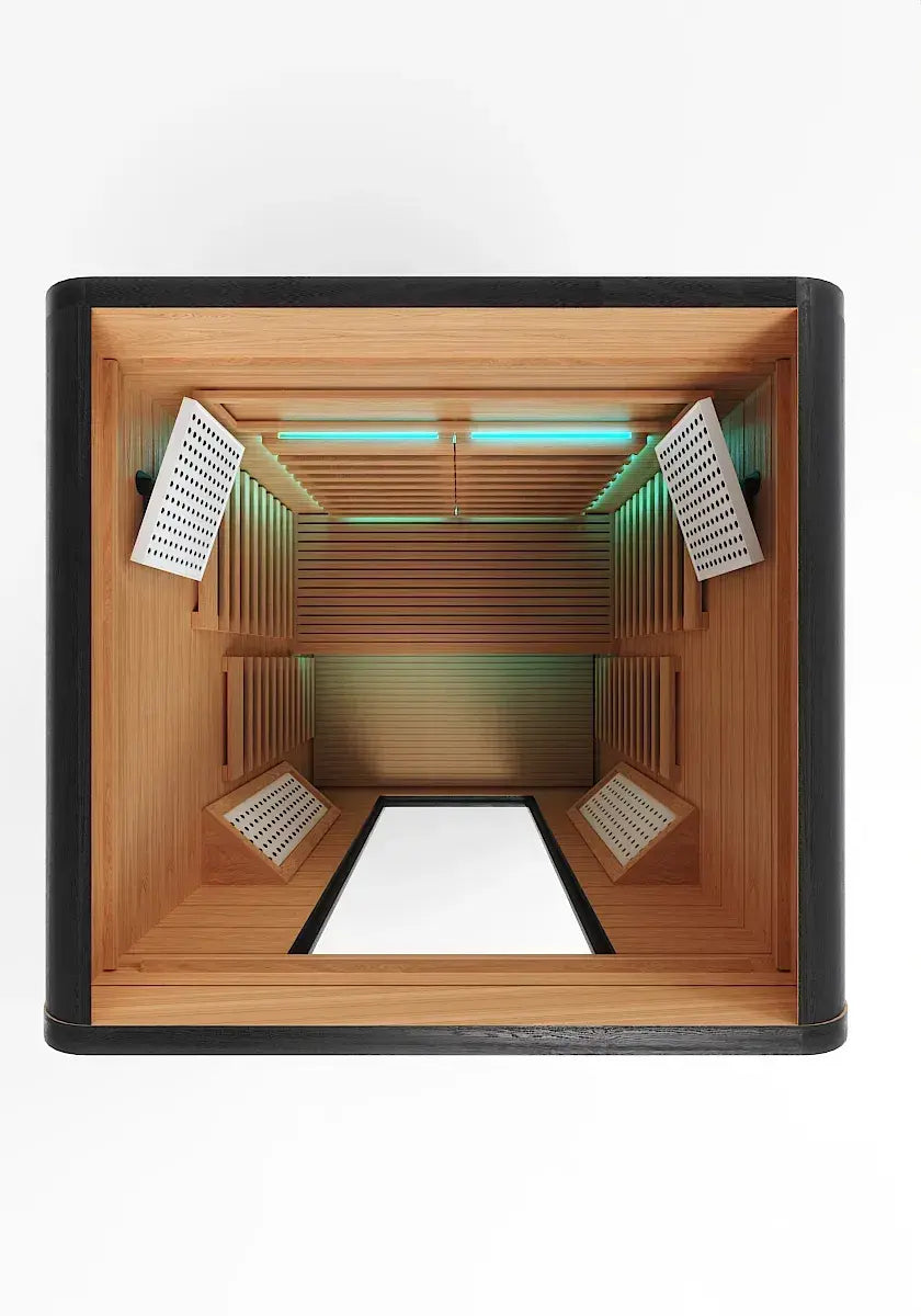 Overhead view of infrared sauna pod interior with cedar wood paneling, cyan light therapy panels on ceiling, and white perforated heating elements mounted on side walls.