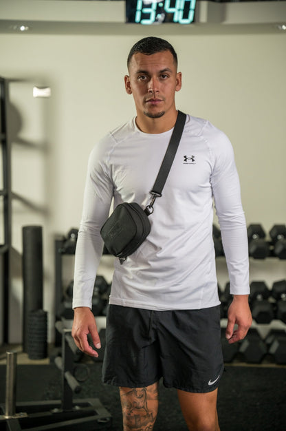 Athletic man in white long-sleeve shirt with crossbody bag at the gym.