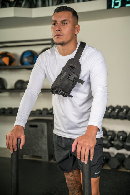 Athletic man in a gym wearing a white long-sleeve shirt and a crossbody chest bag.