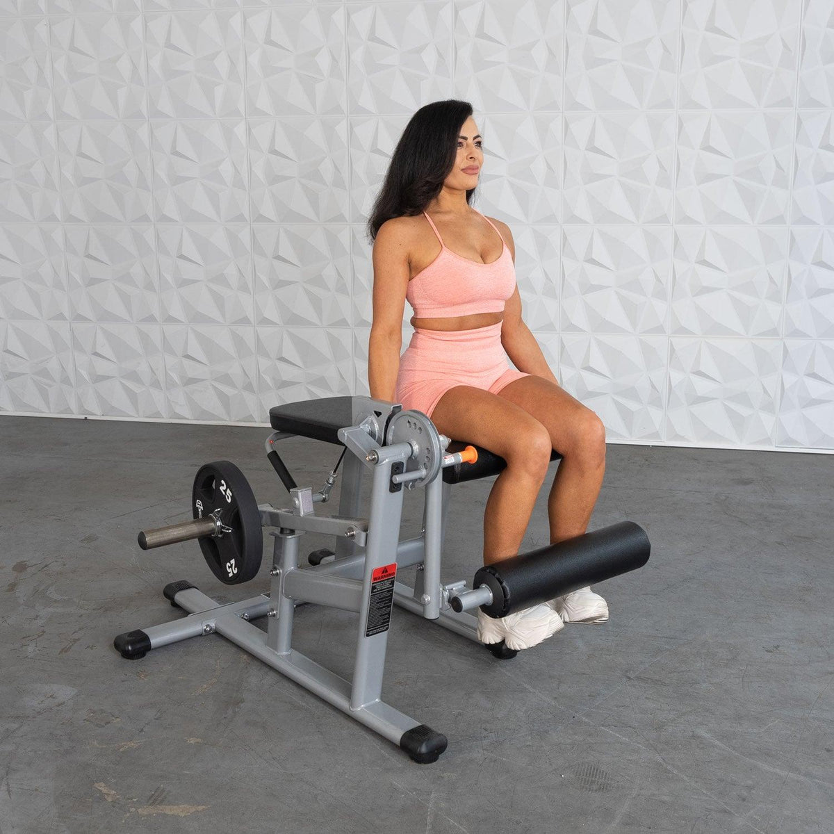 Woman in pink workout outfit seated on leg extension machine.