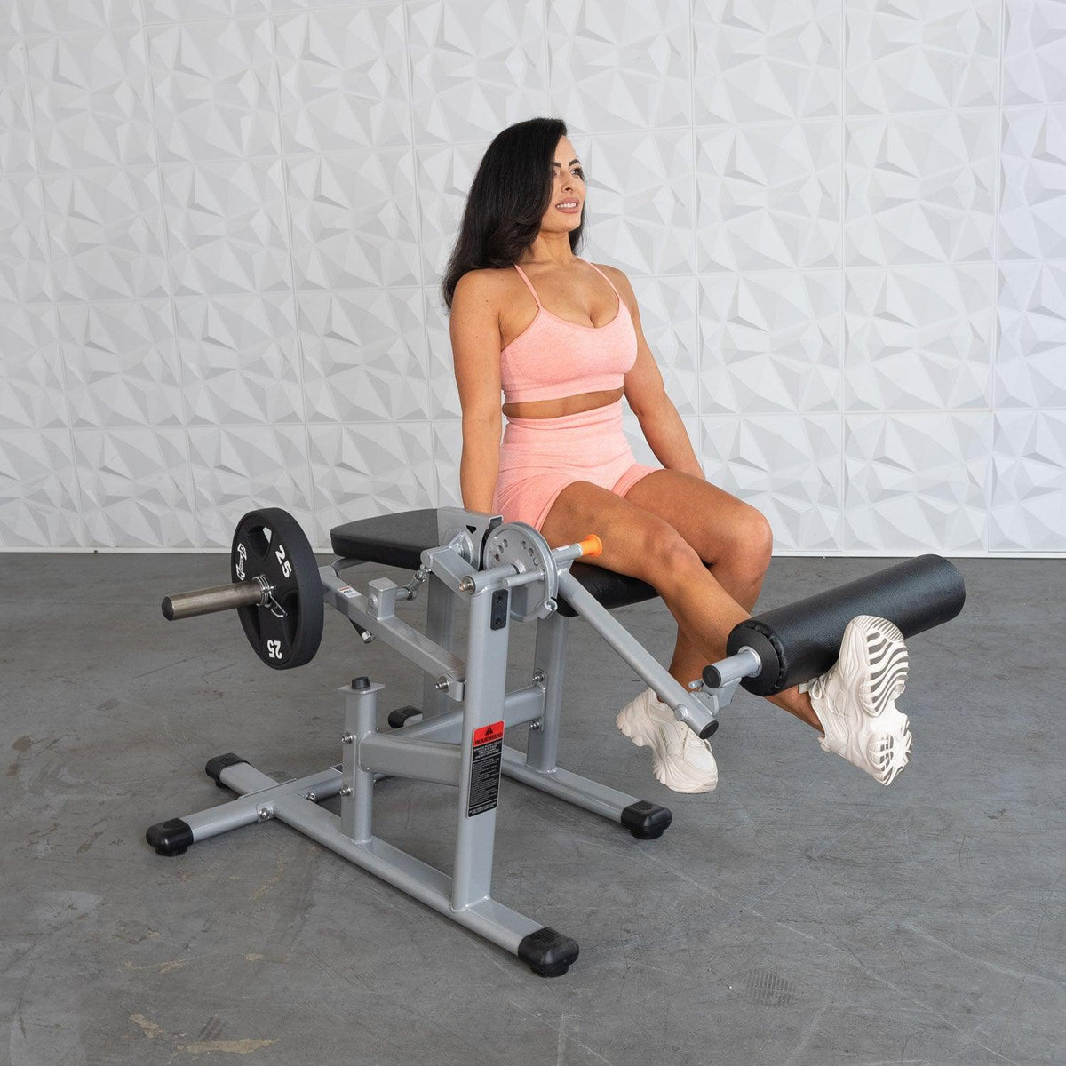 Woman in pink sportswear sits on a leg-extension machine in a gym.