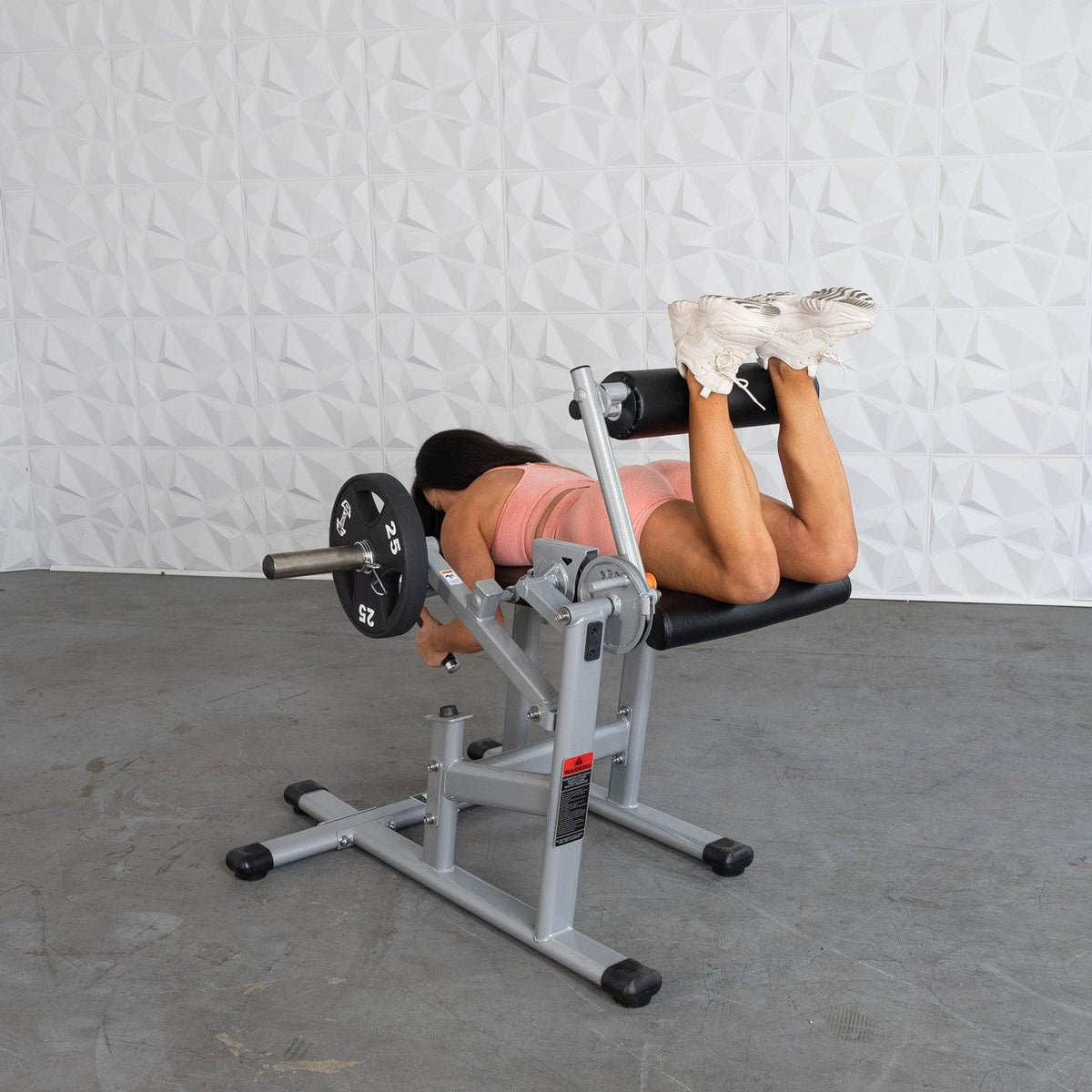 Woman in pink sportswear performing lying leg curl on a weight bench.