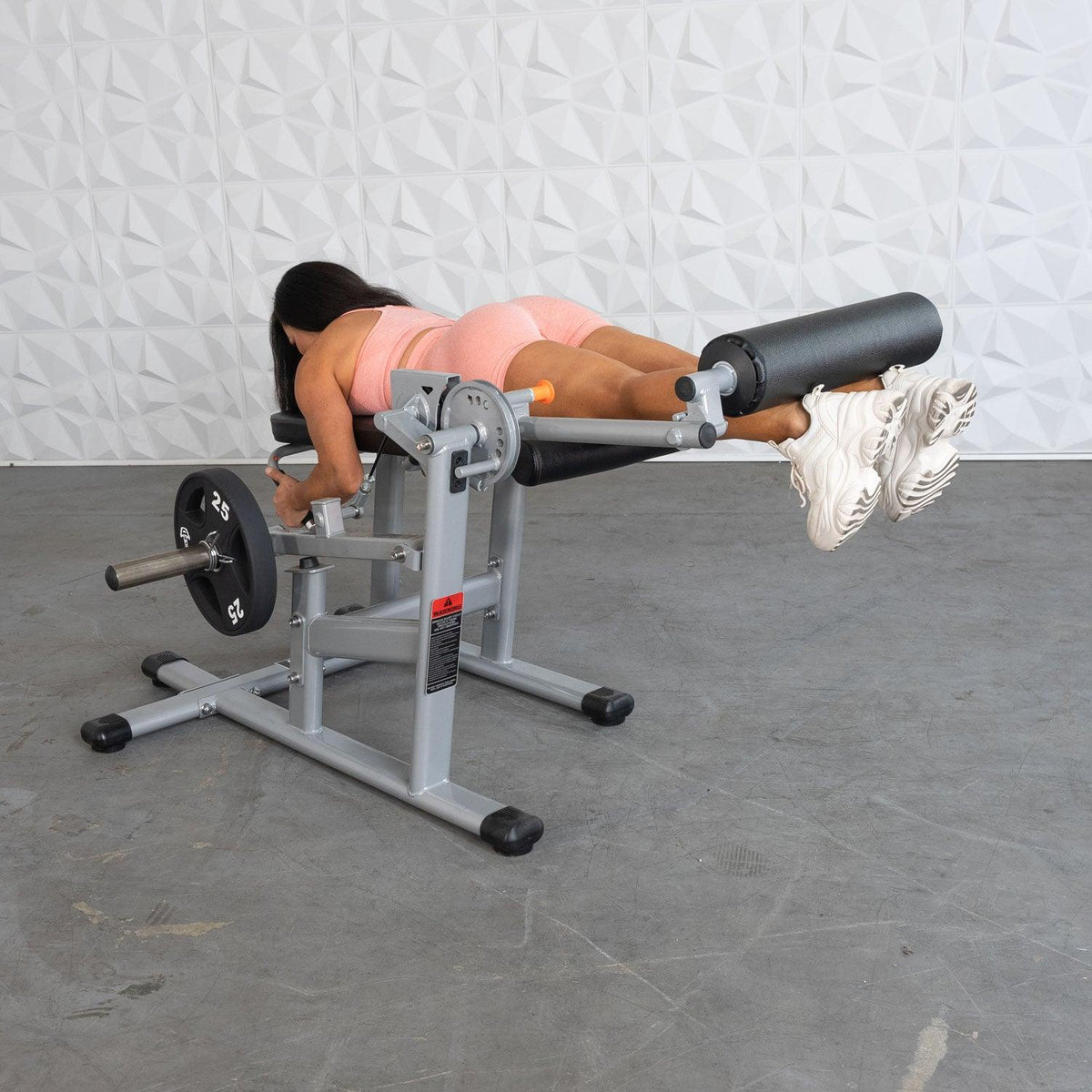 Woman in pink activewear performing leg curl on a weight bench.